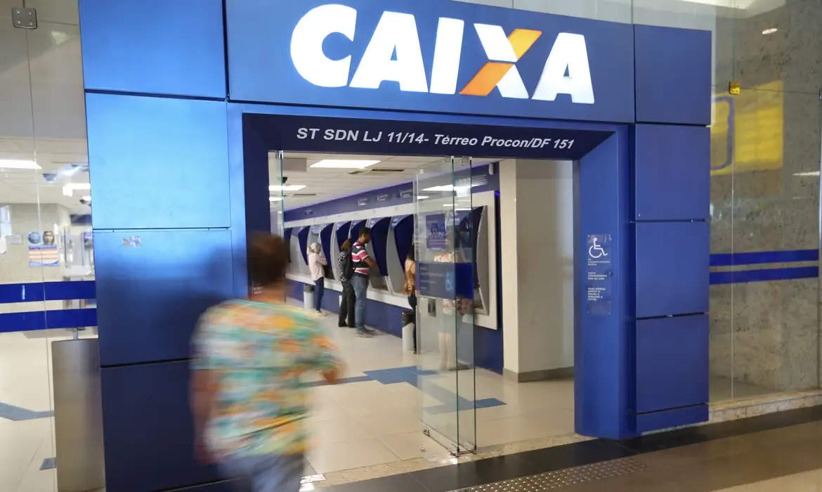 Fachada da agência da Caixa Econômica Federal com pessoas utilizando caixas eletrônicos.