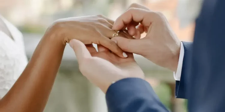 Pessoa colocando aliança no dedo durante cerimônia de casamento.