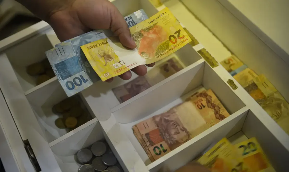Notas de 100 e 20 reais sendo organizadas, simbolizando o pagamento salarial.