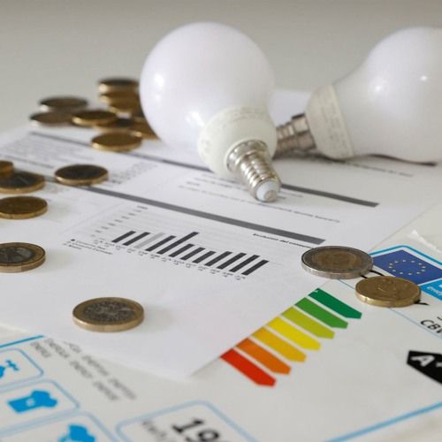 Lâmpadas, moedas e gráfico sobre consumo energético e economia financeira.