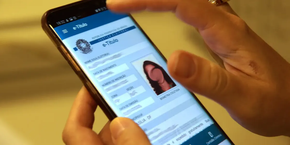 Pessoa acessando o e-Título no celular para verificar a situação eleitoral