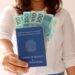 Mulher segurando a carteira de trabalho brasileira com notas de 100 reais visíveis.