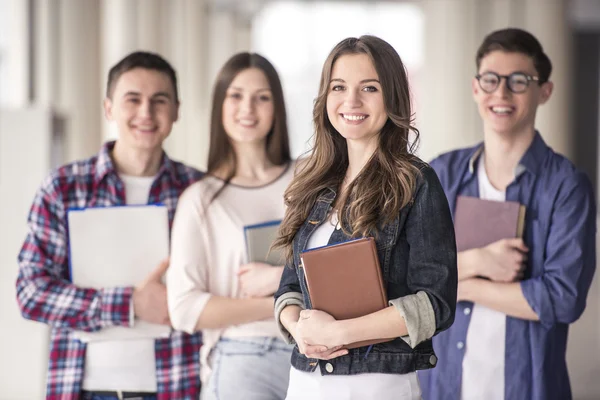 Grupo de estudantes sorrindo e segurando livros em um ambiente acadêmico.