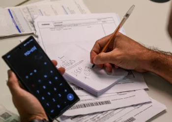 Pessoa usando calculadora no celular para organizar contas e boletos.