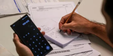 Pessoa usando calculadora no celular para organizar contas e boletos.