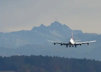 Avião comercial se aproximando para pouso com montanhas ao fundo em um dia nublado.