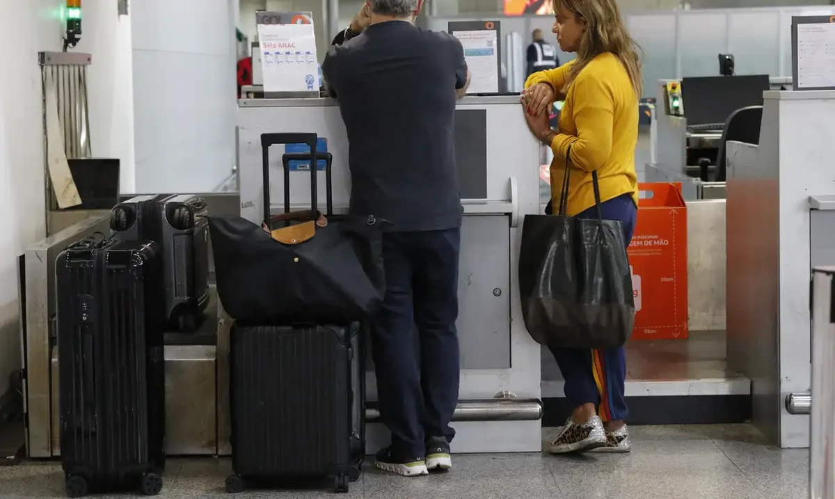 Passageiros aguardando no balcão de check-in com malas pretas ao lado, ilustrando a rotina de viagem aérea.