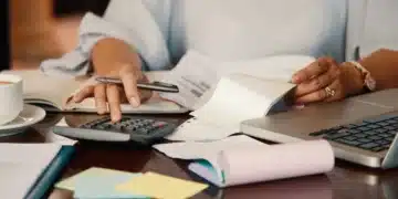 Pessoa calculando contas e organizando documentos financeiros para quitar dívidas e limpar o nome