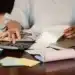 Pessoa calculando contas e organizando documentos financeiros para quitar dívidas e limpar o nome