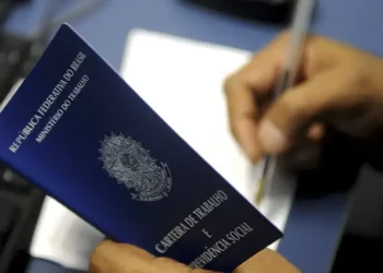 Carteira de trabalho brasileira nas mãos de um trabalhador assinando documento