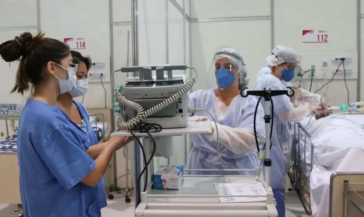 Profissionais da saúde em hospital realizando atendimento em leito de internação.