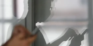 Imagem de uma sombra de uma pessoa refletindo na parede, mostrando as mãos mexendo no celular.
