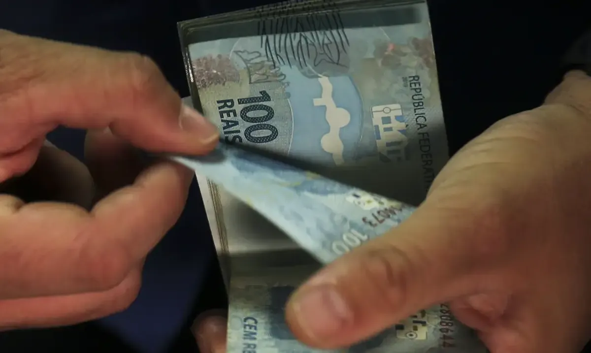 Pessoa retirando uma nota de R$ 100 de uma carteira, representando o direito ao seguro-desemprego.