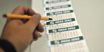 Pessoa marcando números em um bilhete da Mega-Sena com uma caneta laranja.