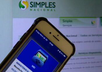 Imagem de um celular exibindo o aplicativo MEI da Receita Federal, com o site do Simples Nacional ao fundo, destacando a importância da declaração anual para MEI.