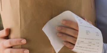 Pessoa segurando uma sacola de papel com alimentos e um recibo de compra visível, simbolizando a importância de pedir a nota fiscal para participar da Nota Premiada MS.