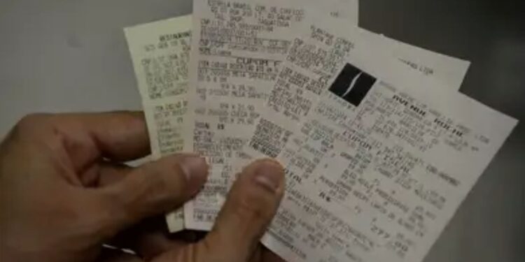 Imagem mostrando um conjunto de cupons fiscais e uma mão segurando-os, relacionado a sorteios de prêmios.