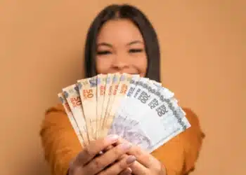 Mulher sorrindo e exibindo uma pilha de notas de 50 e 200 reais, simbolizando os ganhos do programa Nota Paraná.