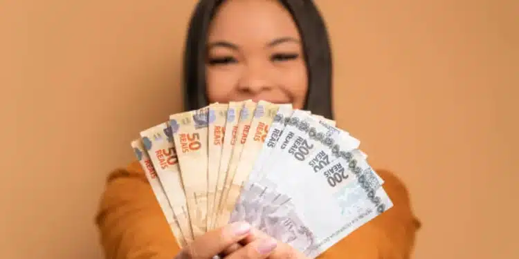 Mulher sorrindo e exibindo uma pilha de notas de 50 e 200 reais, simbolizando os ganhos do programa Nota Paraná.
