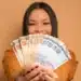 Mulher sorrindo e exibindo uma pilha de notas de 50 e 200 reais, simbolizando os ganhos do programa Nota Paraná.