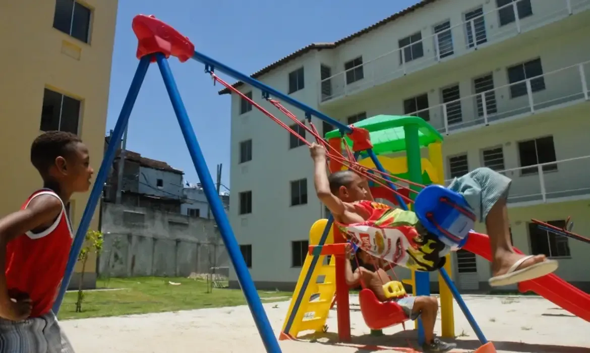  Crianças brincando em parquinho de condomínio habitacional, representando moradia digna.