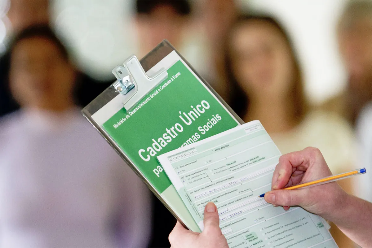 Visita domiciliar do Cadastro Único para programas sociais com formulário sendo preenchido manualmente.