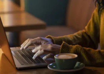 Pessoa trabalhando em um laptop com um café ao lado, representando profissões que permitem ganhar dinheiro de casa.