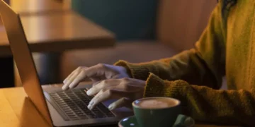 Pessoa trabalhando em um laptop com um café ao lado, representando profissões que permitem ganhar dinheiro de casa.