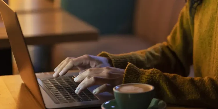 Pessoa trabalhando em um laptop com um café ao lado, representando profissões que permitem ganhar dinheiro de casa.