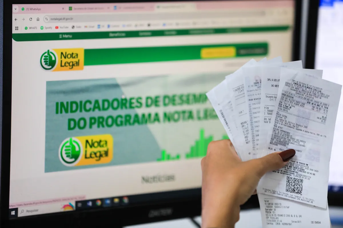 Pessoa segura notas fiscais enquanto acessa o site do Programa Nota Legal no computador