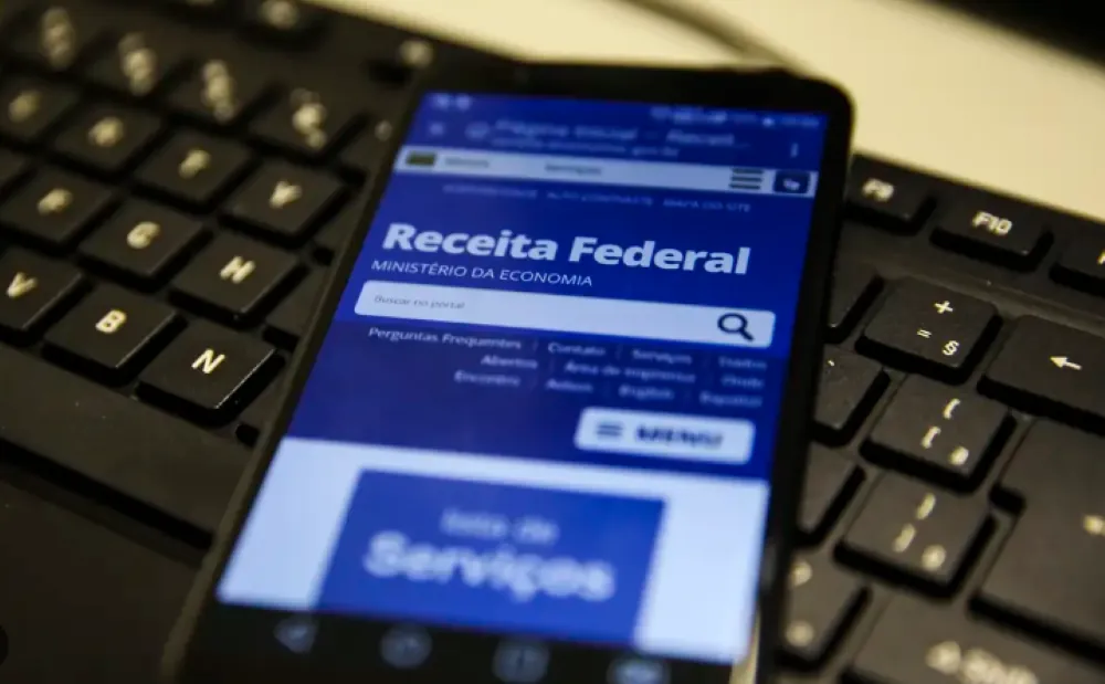 Tela do site da Receita Federal exibida em smartphone, com teclado ao fundo — foco na restituição do IR 2025.