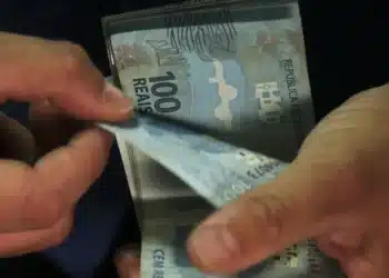 Mãos contando cédulas de 100 reais, ilustrando empréstimo consignado e portabilidade bancária.