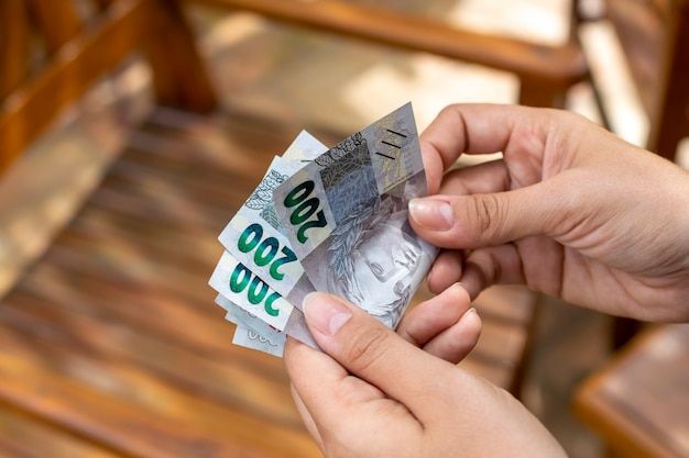 Mão segurando cédulas de R$ 50 e R$ 200, simbolizando o valor do salário mínimo reajustado em 2025.