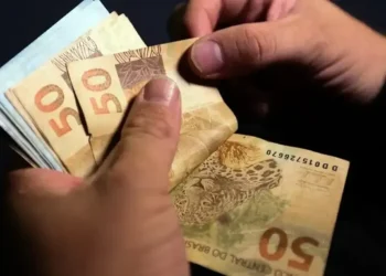 Mãos segurando cédulas de R$ 50, simbolizando o aumento do salário mínimo no estado.