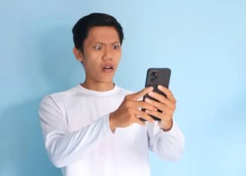 Pessoa surpresa olhando para o celular, representando a reação a um golpe digital.