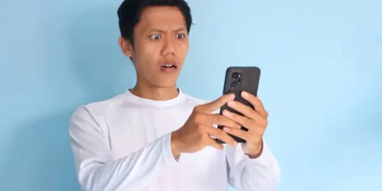 Pessoa surpresa olhando para o celular, representando a reação a um golpe digital.