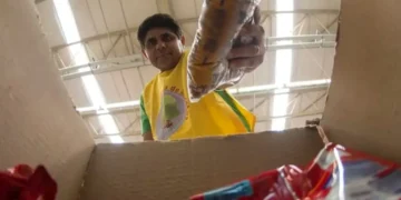 Voluntário entregando cesta básica em caixa de papelão.