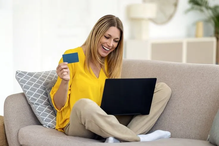 Mulher sorridente fazendo compra online com cartão de crédito, ilustrando tipos de cashback.