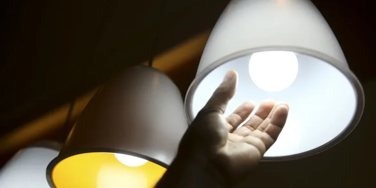 Imagem de uma pessoa ligando uma lâmpada branca, com destaque para a redução do consumo de energia.
