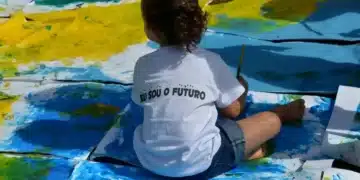 Criança pintando o futuro em uma grande tela, com a frase 'Eu sou o futuro' em sua camiseta.