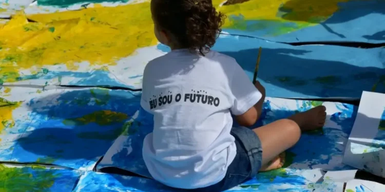 Criança pintando o futuro em uma grande tela, com a frase 'Eu sou o futuro' em sua camiseta.