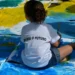 Criança pintando o futuro em uma grande tela, com a frase 'Eu sou o futuro' em sua camiseta.