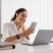 Mulher com celular e laptop sorrindo, simbolizando o trabalho remoto e online.