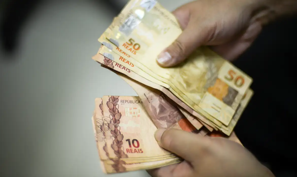 Mão segurando dinheiro em espécie, ilustrando o pronunciamento do governo sobre os pagamentos.