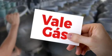 Cartão Vale Gás Social sendo segurado, com fundo de botijões de gás.