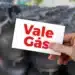 Cartão Vale Gás Social sendo segurado, com fundo de botijões de gás.
