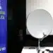 Antena parabólica digital com equipamentos e banner de campanha sobre a mudança para o sinal digital de TV, promovendo a melhoria da qualidade de som e imagem.