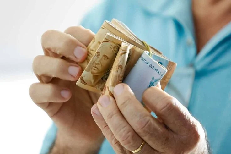 Pessoa segurando notas de R$50, R$100 e outras cédulas de reais, representando o impacto do benefício financeiro do programa Devolve ICMS.
