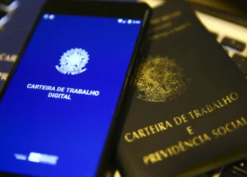 Carteira de Trabalho Digital e física sobre teclado, representando benefícios trabalhistas e a possibilidade de solicitar apoio financeiro em caso de perda de emprego.