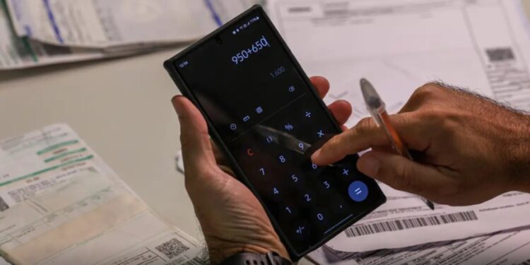 Pessoa usando calculadora no celular para somar valores de contas bancárias e boletos acumulados.